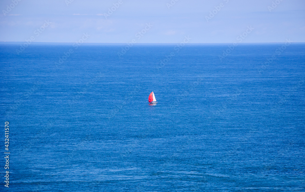 A sailboat with red and white sails in the calm sea. (Brittany, France) Dreams come true concept.
