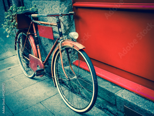 Rusty vintage red bicycle leaning with on red wooden board (useful for entering a text advertisement, menu etc) and carrying plants in wooden box as decoration. Retro aged photo.