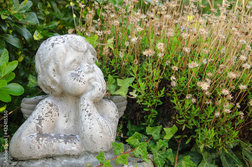 Weathered statue of an infant angel in overgrown garden.