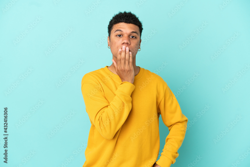 Young African American man isolated on blue background covering mouth with hand Young African American man isolated on blue background covering mouth with hand