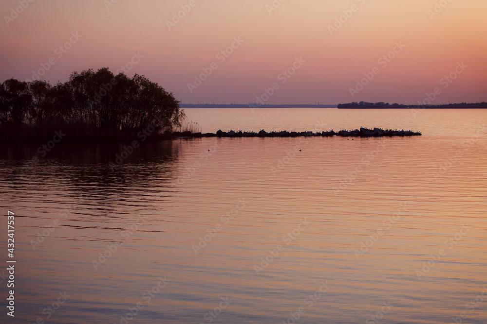 Coast pond. Water surface. Calm. Sunny weather. River bank. Textured background. Orange sunset in warm colors. Golden hour.