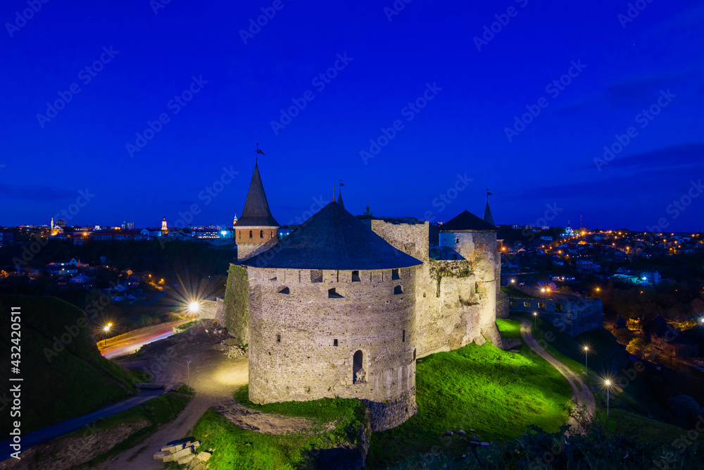View on the Kamianets-Podilskyi сastle in the evening. Beautiful stone castle on the hill on the sunset. Clouds in the darkening sky above the castle. Blue hour. Ukraine