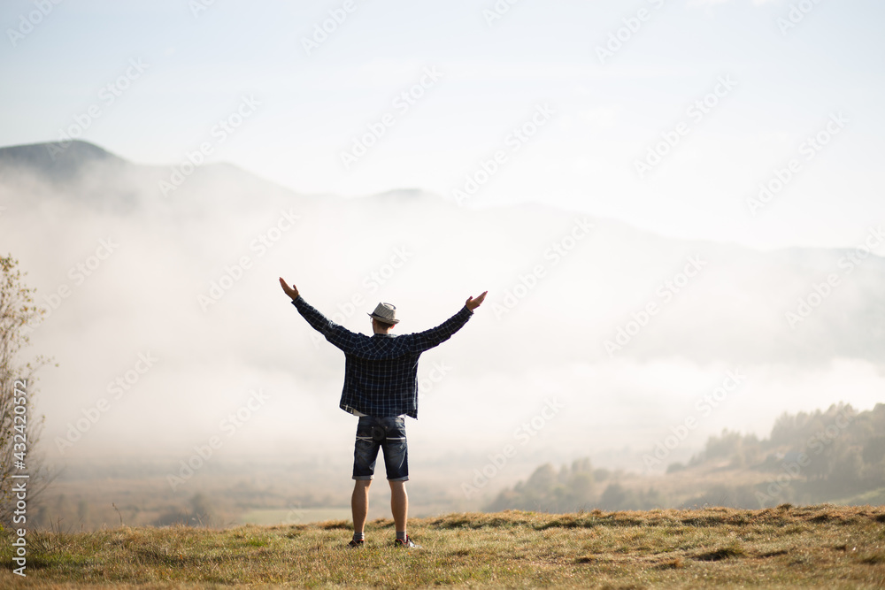Happy traveler man raising hands up on the top of the world above mountains in white clouds. Hipster guy enjoy amazing atmospheric moment. travel and wanderlust concept Happy traveler man raising hands up on the top of the world above mountains in white clouds. Hipster guy enjoy amazing atmospheric moment. travel and wanderlust concept