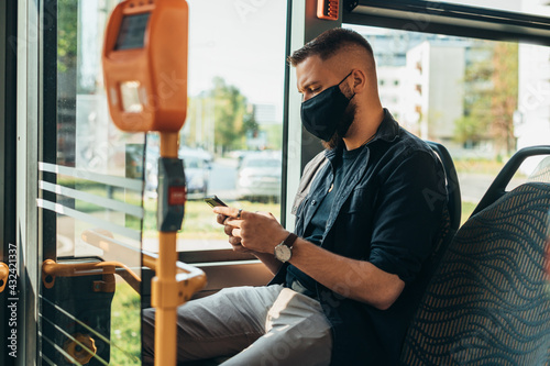 Young man using smartphone and wearing a protective mask in a bus