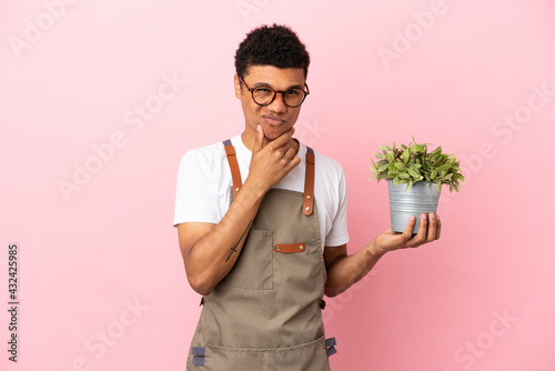 Gardener African man holding a plant isolated on pink background thinking