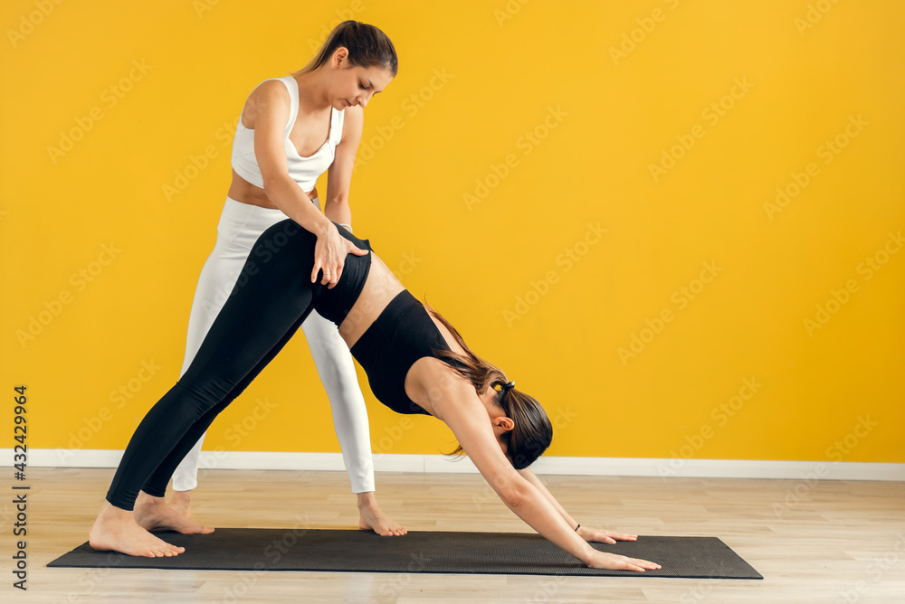 A female yoga coach controls the performance of a pose, asana. Stretching with a trainer