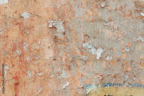A red-yellow fragment of a concrete wall with a copious amount of scratches. Rough surface with scuffs and cracks. Remains of announcements: glue and paper.