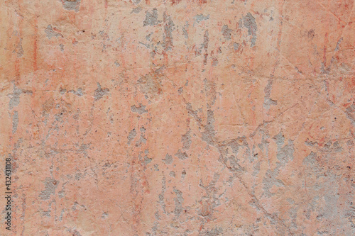 A red-yellow fragment of a concrete wall with a copious amount of scratches. Rough surface with scuffs and cracks.