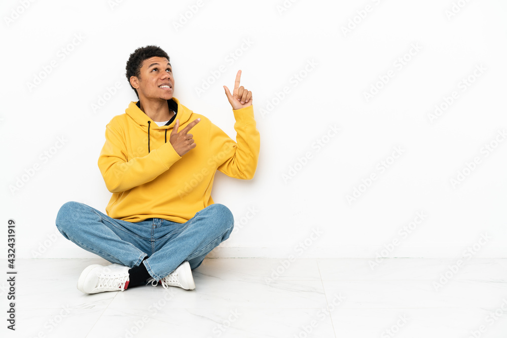 Young African American man sitting on the floor isolated on white background pointing with the index finger a great idea