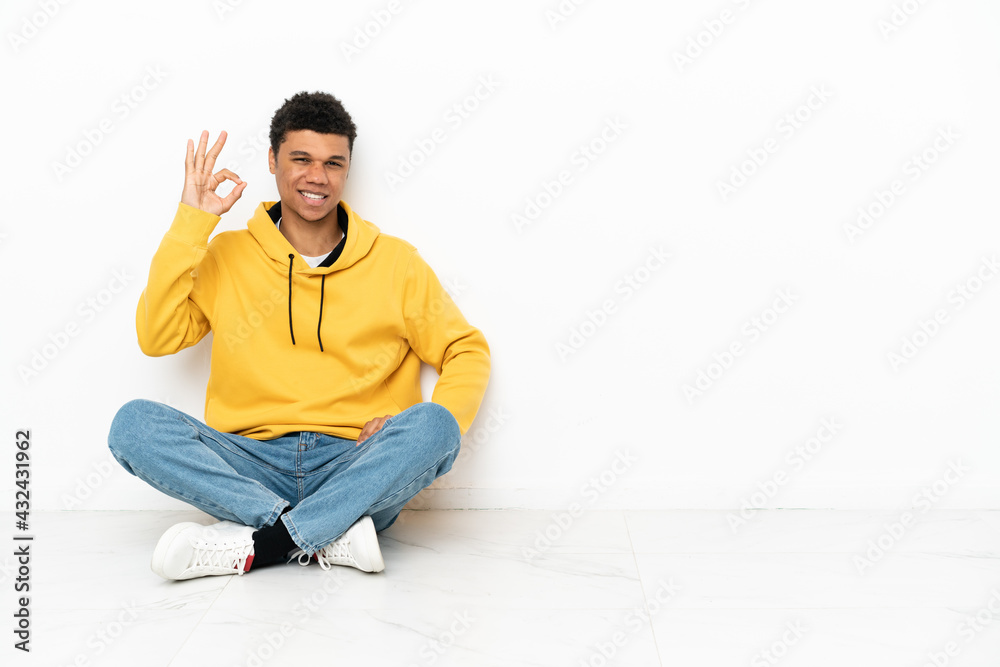 Young African American man sitting on the floor isolated on white background showing ok sign with fingers