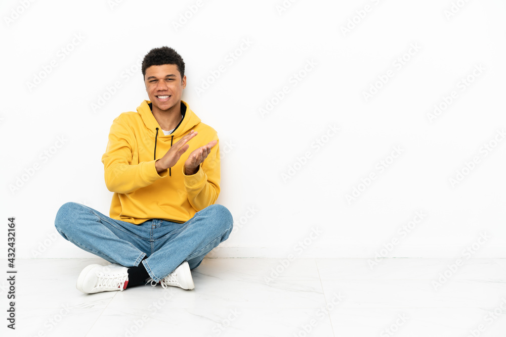 Young African American man sitting on the floor isolated on white background applauding after presentation in a conference