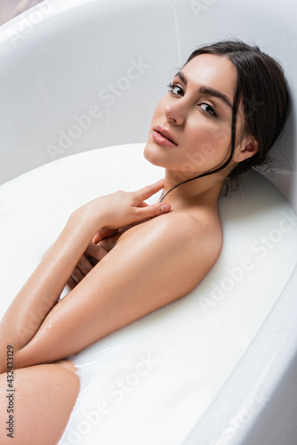 sensual woman in milk bath touching neck while looking at camera.