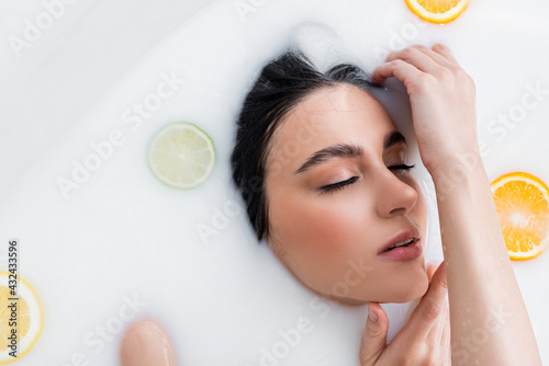 overhead view of young woman with closed eyes taking milk bath with citrus slices.