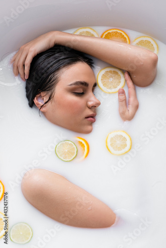 young woman bathing in milk with fresh, sliced citruses.