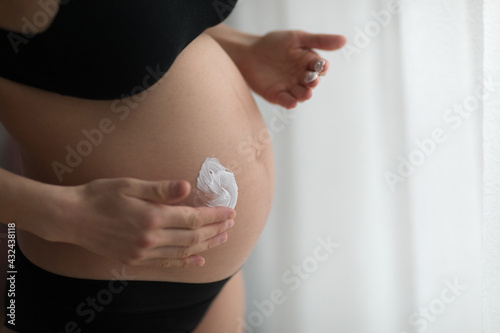 Pregnant women putting anti stretch creme on her belly. Cosmetic for moisturizing or hydrating skin in pregnancy. photo