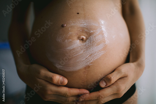 Pregnant women putting anti stretch creme on her belly. Cosmetic for moisturizing or hydrating skin in pregnancy.