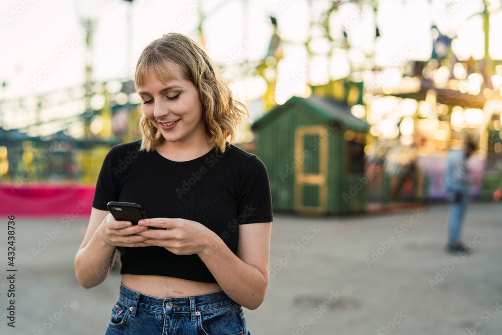 Chica rubia joven tomándose selfies en zona de atracciones de una feria