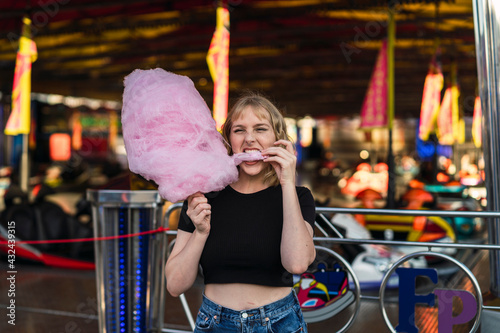 Chica rubia guapa comiendo algodón de azúcar en zona de atracciones de una feria