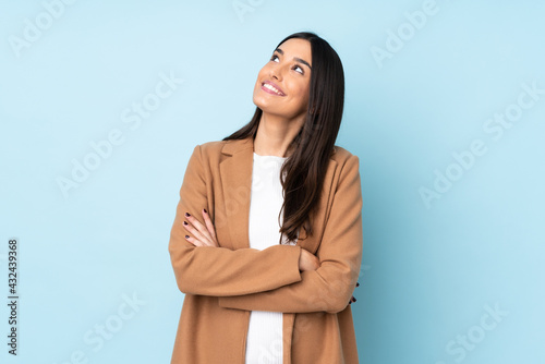 Young caucasian woman isolated on blue background looking up while smiling photo