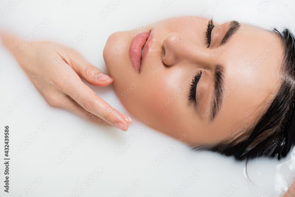 Naklejka premium young woman holding hand near face while bathing in milk.