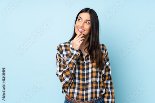 Young caucasian woman isolated on blue background looking up while smiling © luismolinero