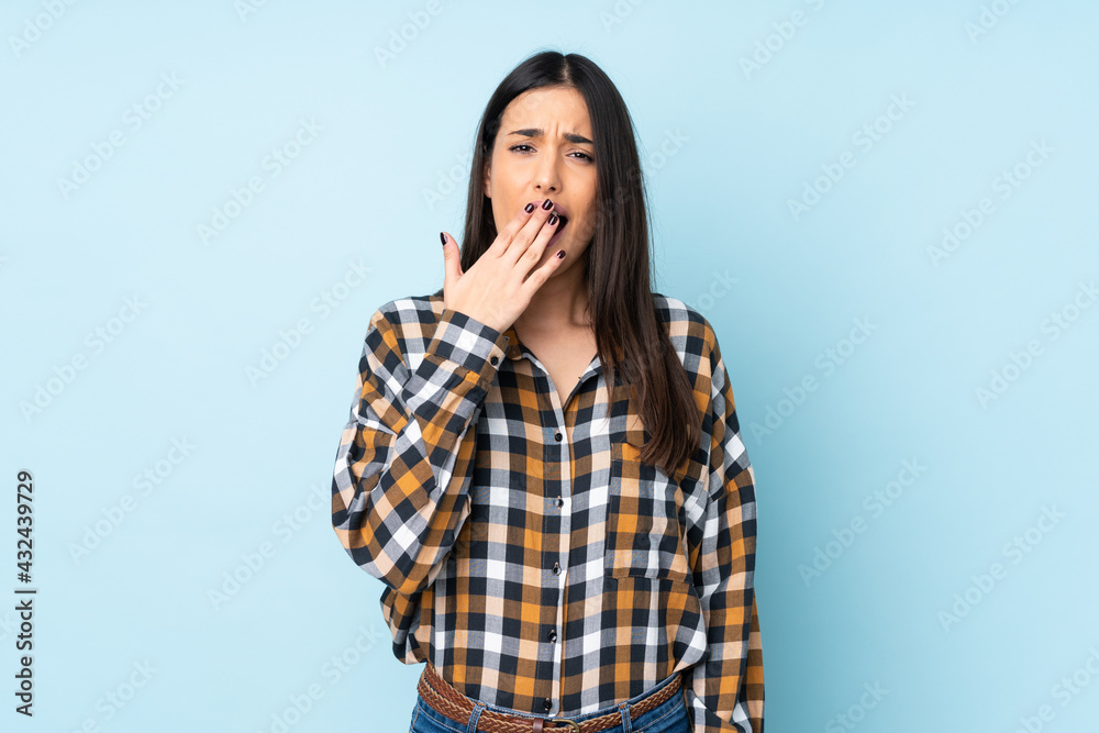 Young caucasian woman isolated on blue background yawning and covering wide open mouth with hand