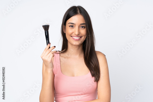 Young caucasian woman isolated on white background holding makeup brush and whit happy expression