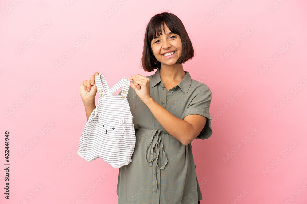 Woman over isolated background pregnant and holding baby clothes Woman over isolated background pregnant and holding baby clothes