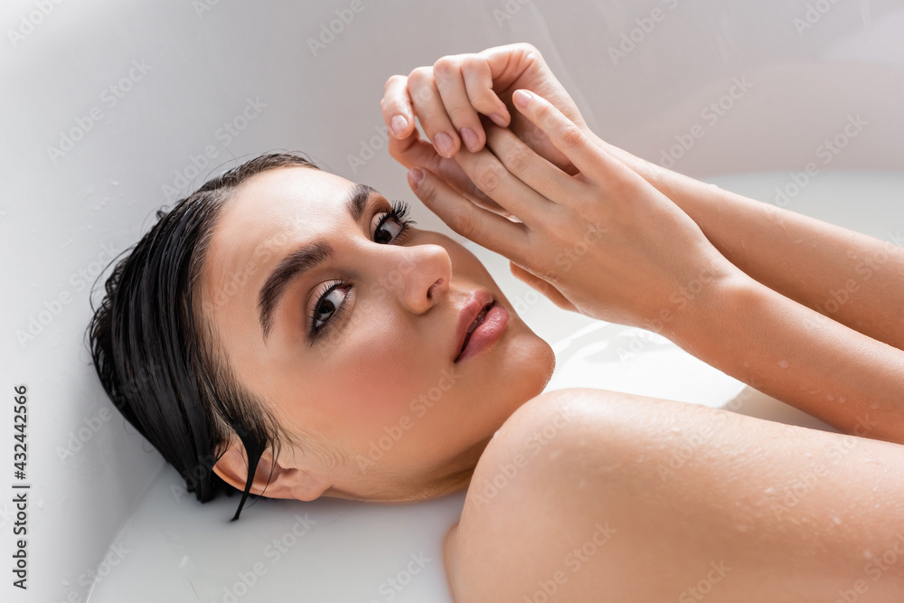 Naklejka premium pretty woman holding hands near face while relaxing in bath with milk.