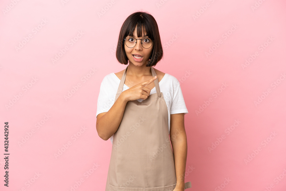 Restaurant waiter over isolated pink background surprised and pointing side Restaurant waiter over isolated pink background surprised and pointing side