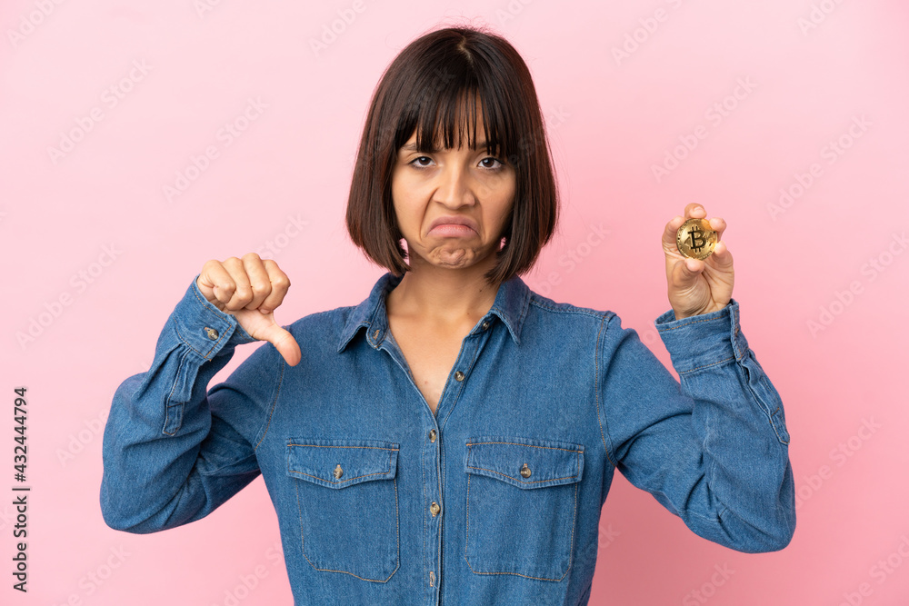 Young mixed race woman holding a Bitcoin isolated background showing thumb down with negative expression Young mixed race woman holding a Bitcoin isolated background showing thumb down with negative expression