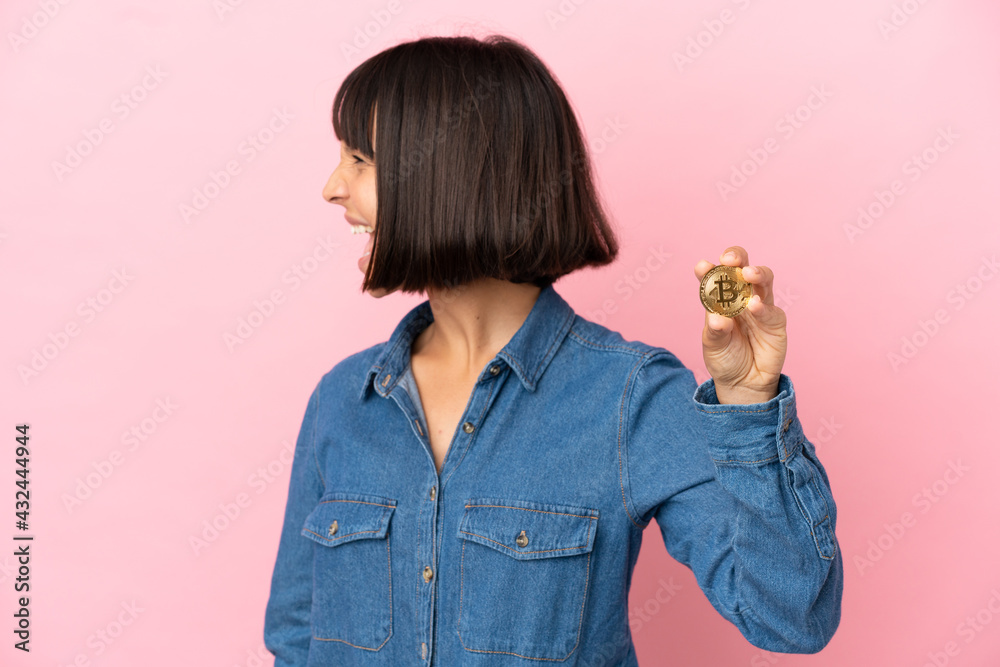 Young mixed race woman holding a Bitcoin isolated background laughing in lateral position