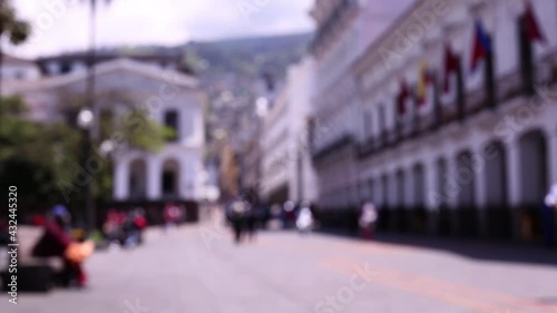 Defocused footage with blurred people walking over a large square in a city with flags hanging on the walls at the side