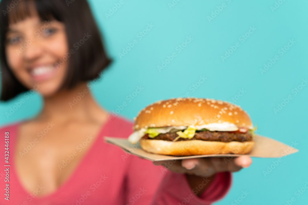 Young brunette woman holding a burger over isolated background Young brunette woman holding a burger over isolated background