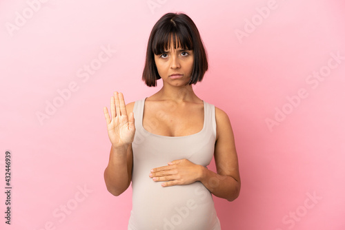 Young pregnant woman over isolated pink background making stop gesture