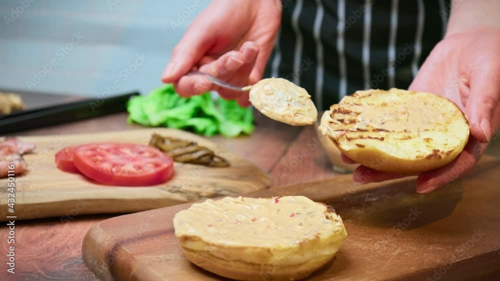Spreading sauce from mayo, ketchup, mustard on top of a toasted burger bun in 4K. Concept of spreading burger sauce on a grilled bread bun. Spreading sauce from mayo, ketchup, mustard on top of a toasted burger bun in 4K. Concept of spreading burger sauce on a grilled bread bun.