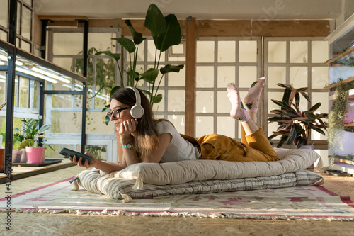 Fotografija Female gardener relax after work lay on floor, listen music and surfing internet on smartphone app in cozy living room