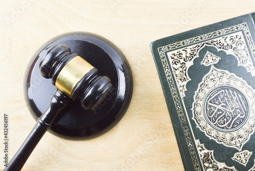 Top view image of holy Quran with law gavel on wooden background. Sharia or Islamic law concept. Large arabic word mention the holy Quran is with variance recitations. photo