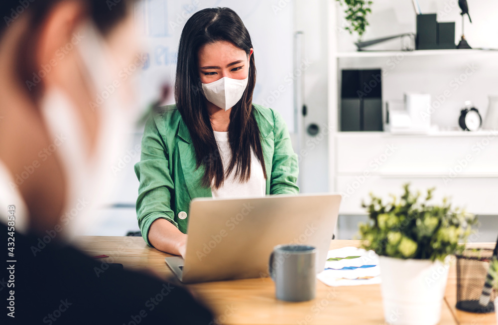 Young asian business woman using laptop computer working and planning meeting in quarantine for coronavirus wearing protective mask with social distancing while sitting on office desk Young asian business woman using laptop computer working and planning meeting in quarantine for coronavirus wearing protective mask with social distancing while sitting on office desk