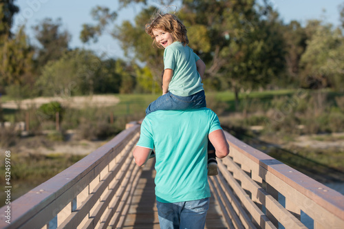 фотографія Father carrying son on shoulders on walk in Park. Back view.