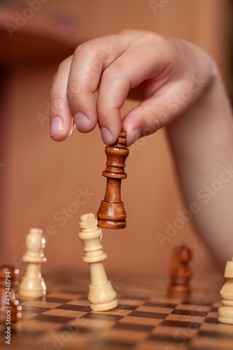 child hand holds chess piece of black king and knocks down opponent's piece- white king