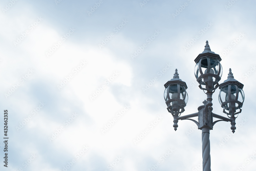 Vintage lantern on the street, against the backdrop of a cloudy sky. Three lamps on a decorative pole. Copy space