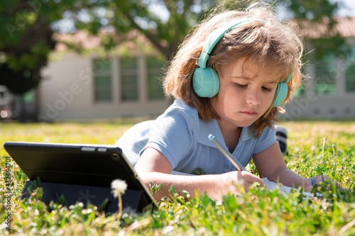 Child homework outside in scholl yard. Little schoolboy pupil with tablet in the park on grass. Self education, kid learning and studying on school park. Early development for children. photo