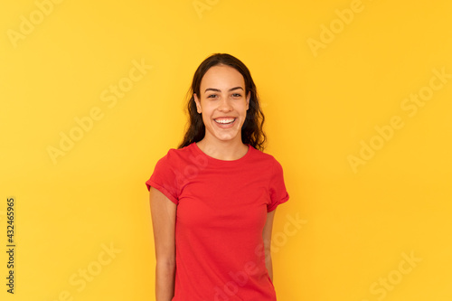 Cheerful young latina woman, wears red t-shirt, isolated over yellow background. People, emotions and style concept