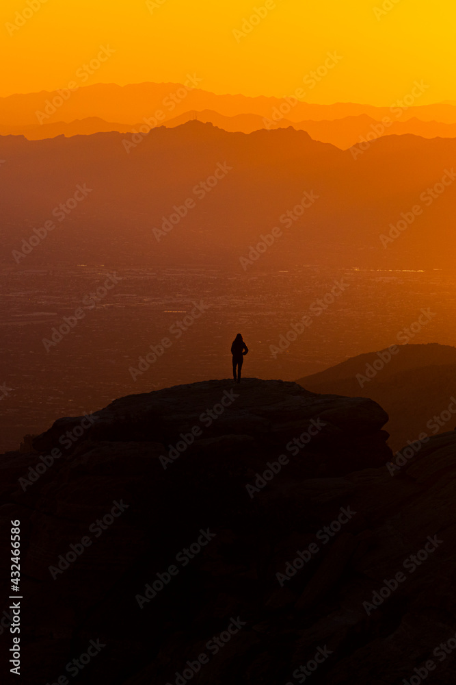 A figure watches the sun set over layers of mountains