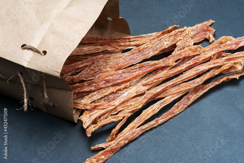 Sliced turkey or chicken meat dehydrated and packed into craft brown paper. Homemade natural dry dog treats. Dark background, copy space.