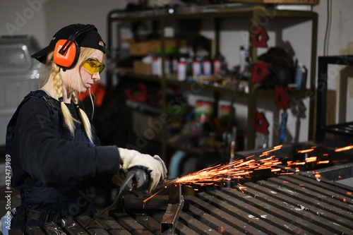 Fotografia, Obraz Photo of young woman with angle grinder working in protection in garage