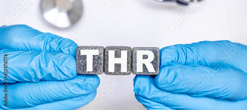 THR Total hip replacement - word from stone blocks with letters holding by a doctor's hands in medical protective gloves