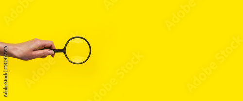 female hand holds a magnifying glass loupe on a yellow background. Banner