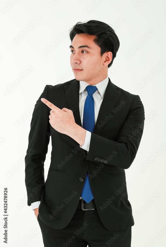 Young successful businessman in a formal black suit is looking and pointing his finger away while standing on white background Young successful businessman in a formal black suit is looking and pointing his finger away while standing on white background